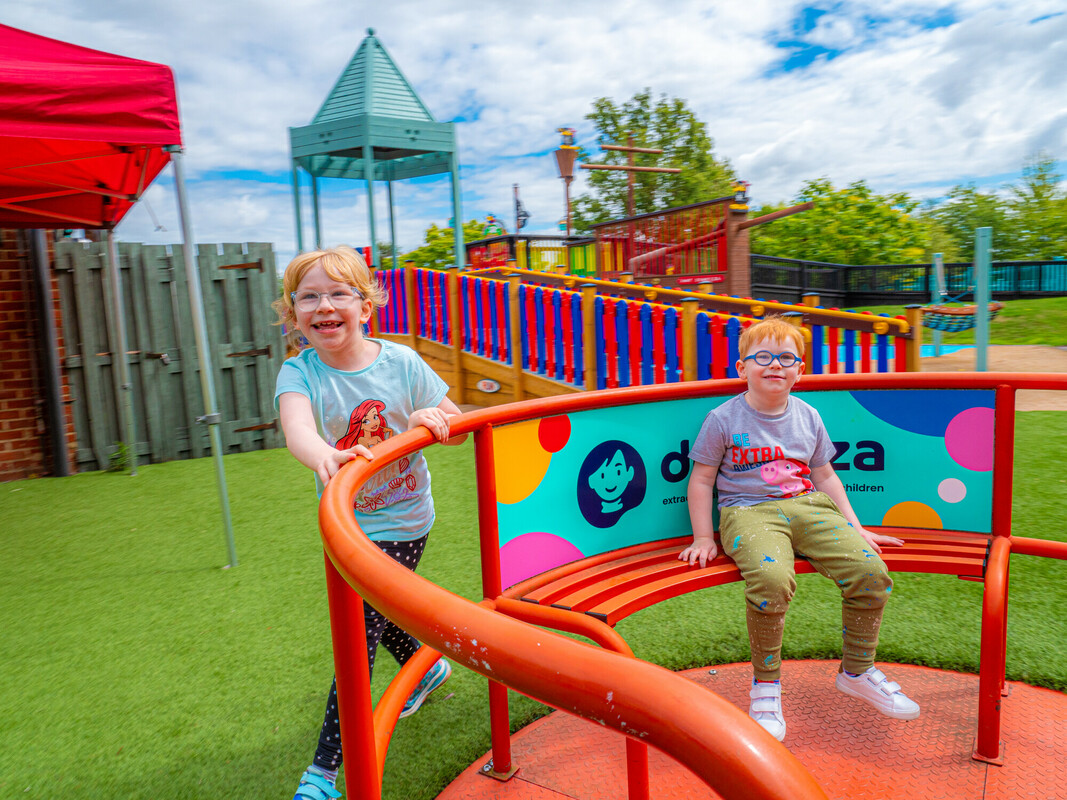Poppy and Arthur smiling and playing together in a brightly coloured playground in Kent.