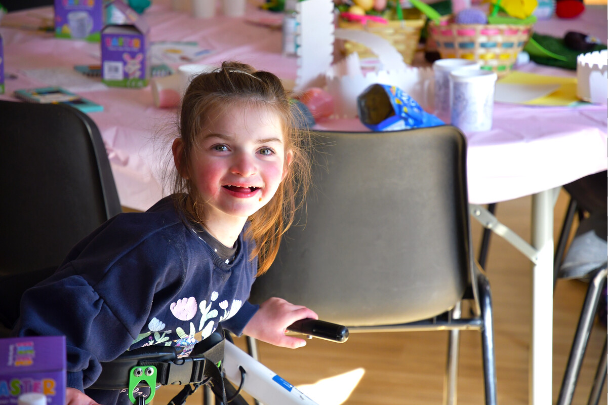 Lola smiling while seated at the East Sussex Spring Get Together 2025, with a crafting table in the background.