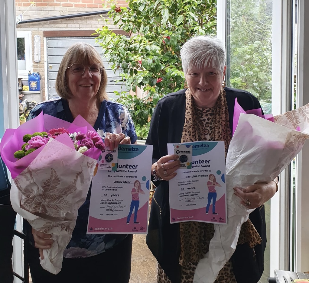Two women holding bouquets and certificates for 30 years of volunteer service, awarded by Demelza.