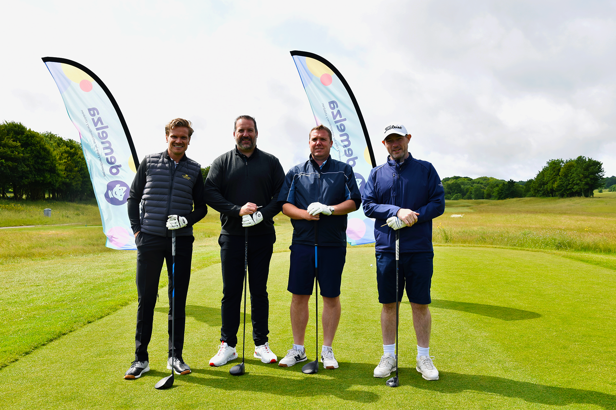 Four men standing with golf clubs in front of Demelza banners at the London Golf Club for the Demelza Golf Day