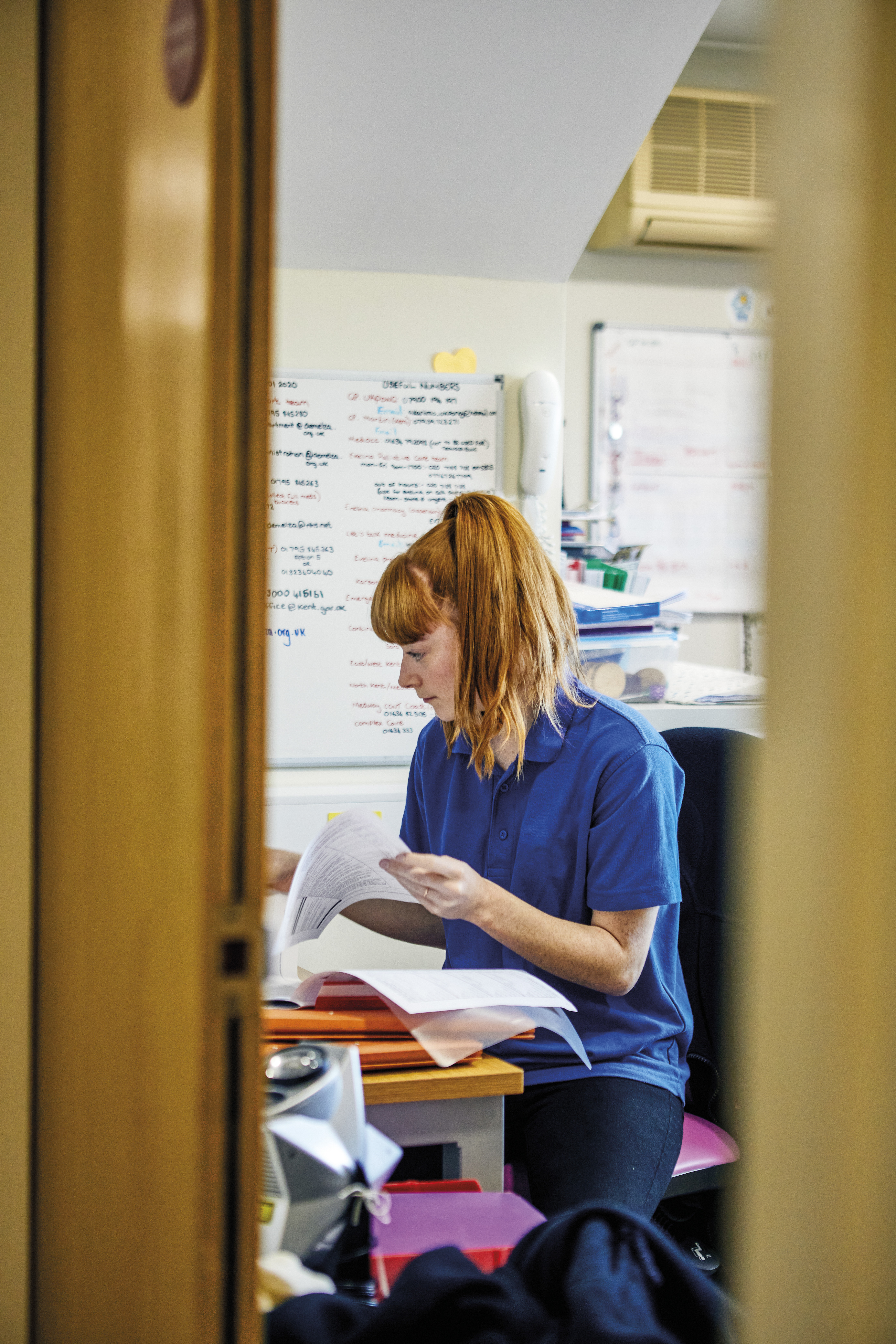 A nurse with ginger hair sitting down at a desk doing admin work