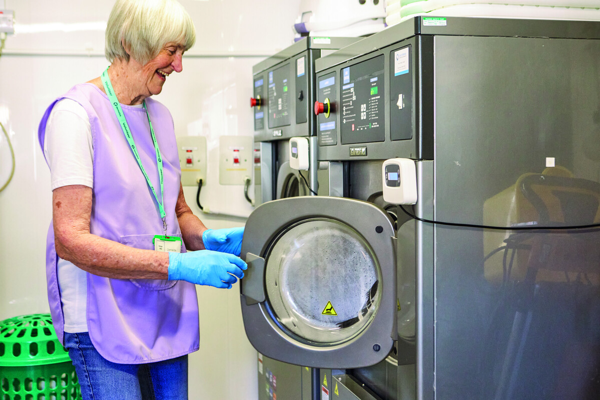 Hospice volunteer Lyn standing at a washing machine, tending to laundry duties.