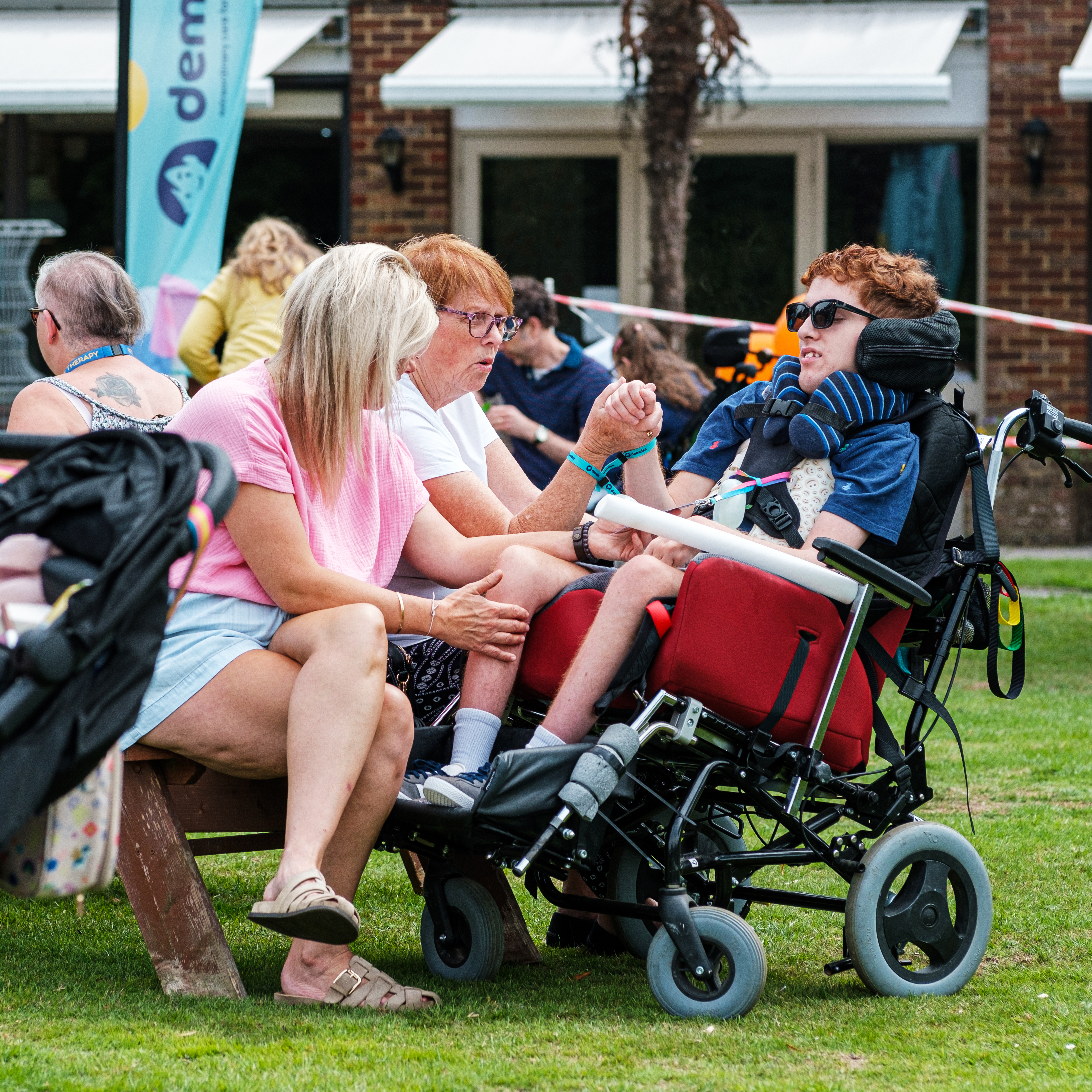 A young person with ginger hair in a wheelchair with his family at a Demelza event
