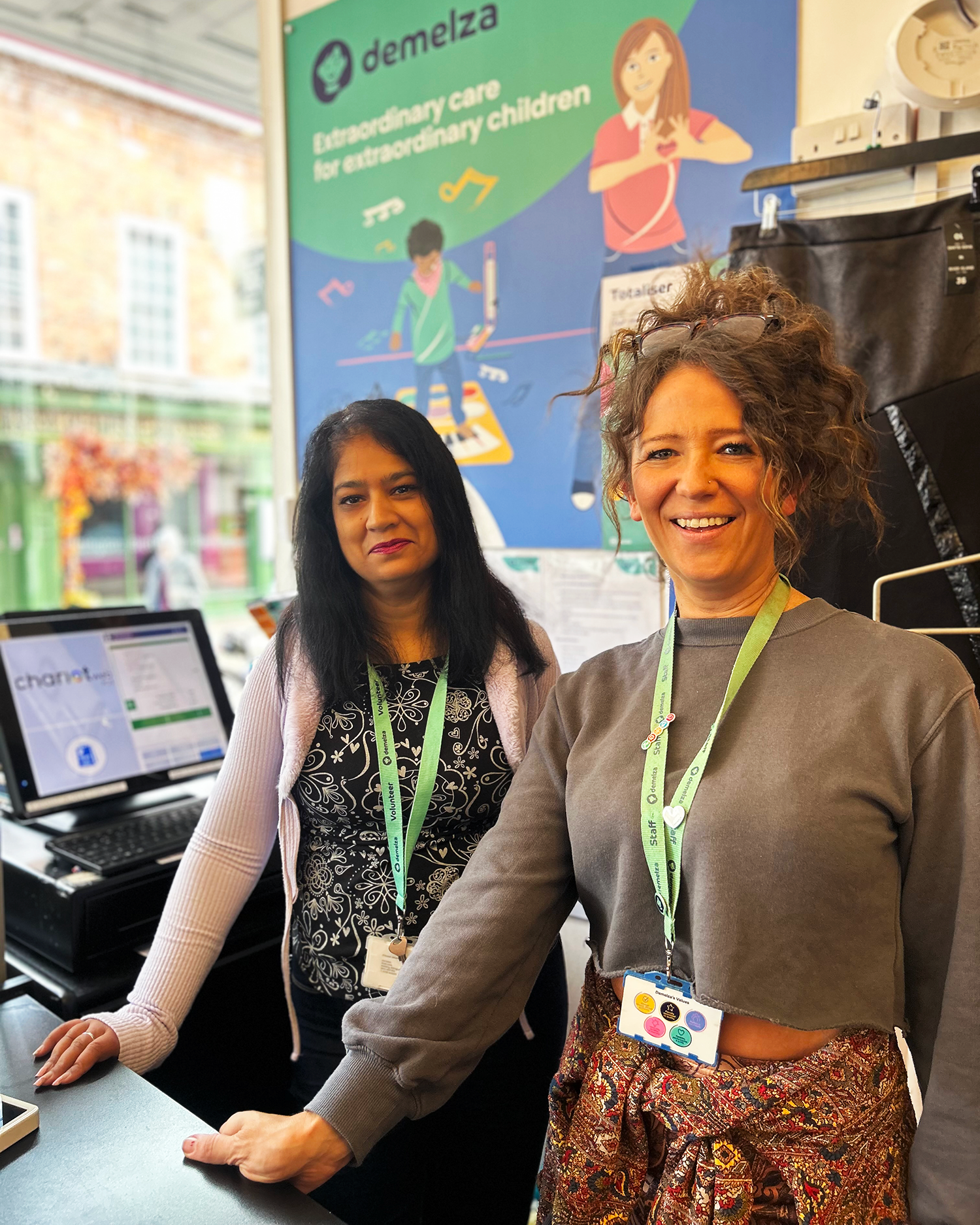Two ladies smiling to camera behind the till in a charity shop