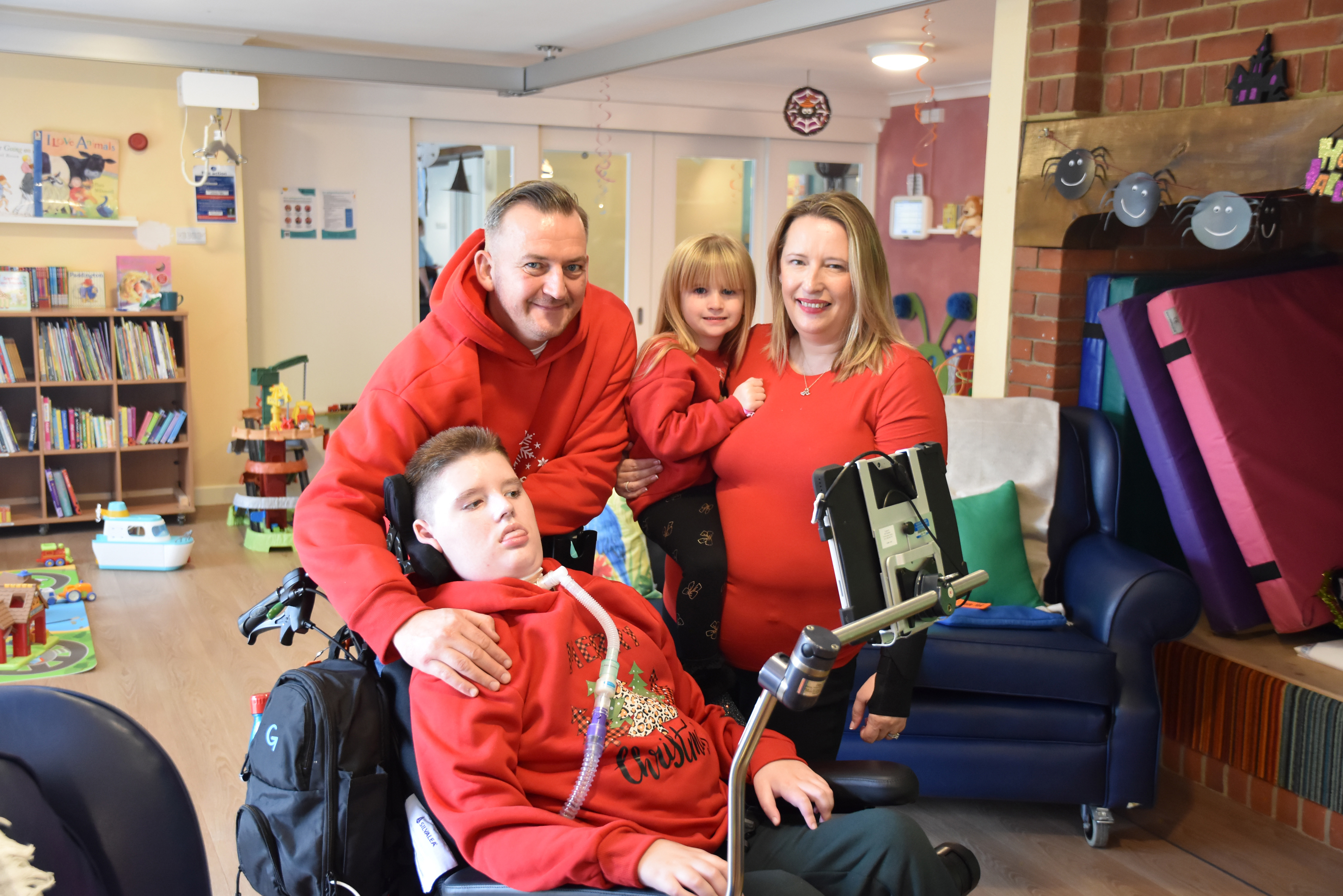 Mum, dad, sister and son in a wheelchair in a play room smiling to camera