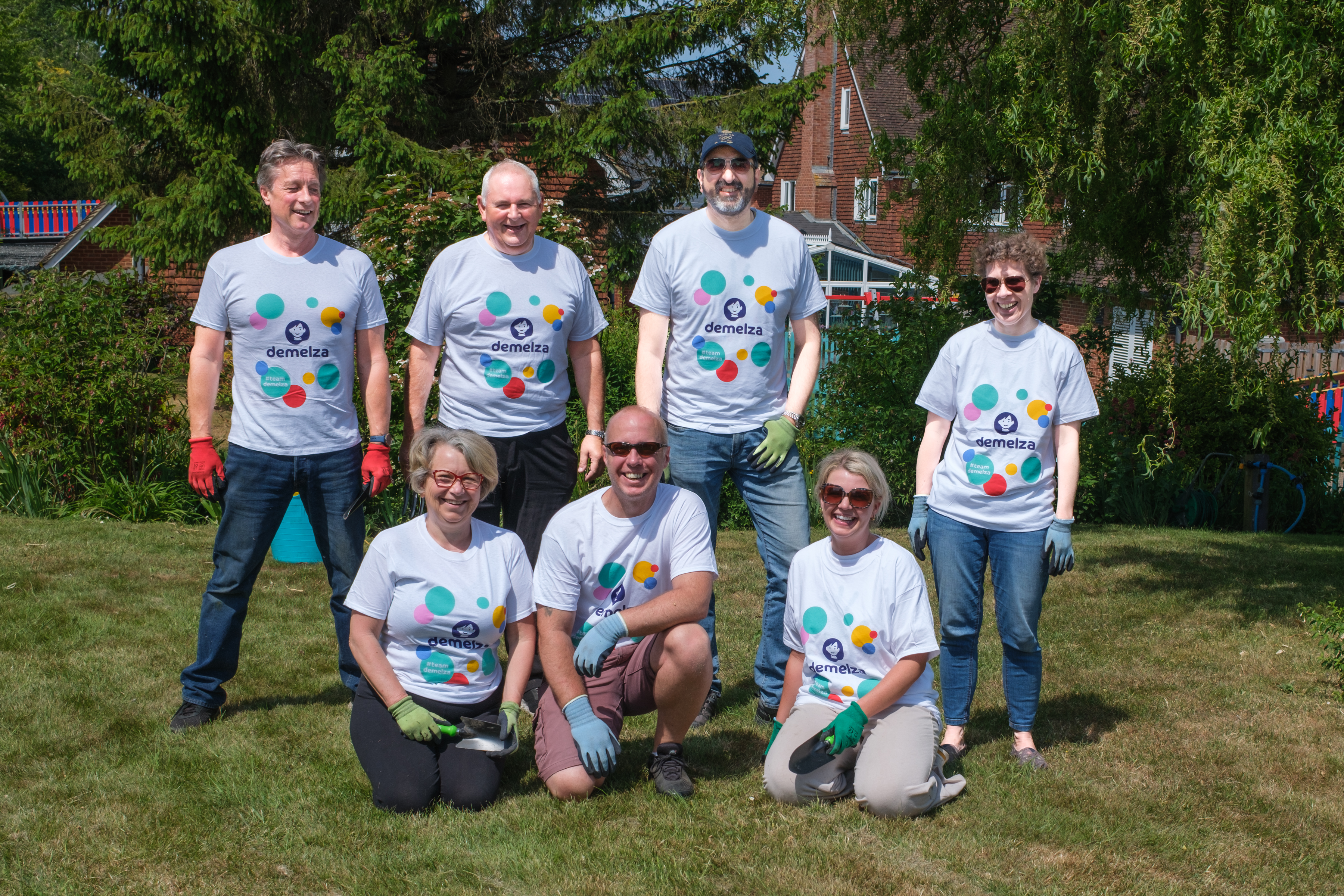 Clarins corporate volunteers wear Demelza tops and smile together in a sunny garden.