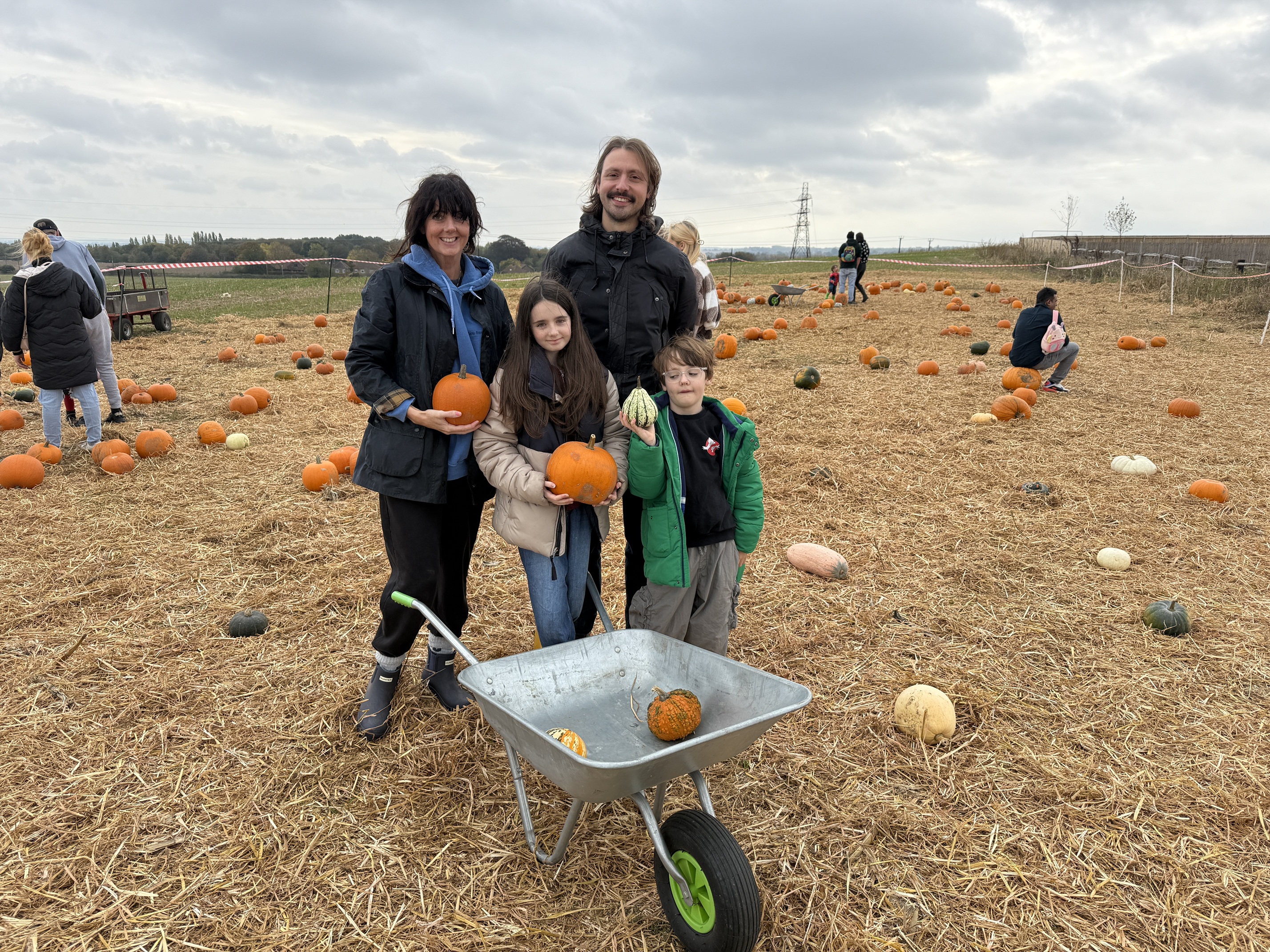 Family holding pumpkins and a wheelbarrow in a field of pumpkins