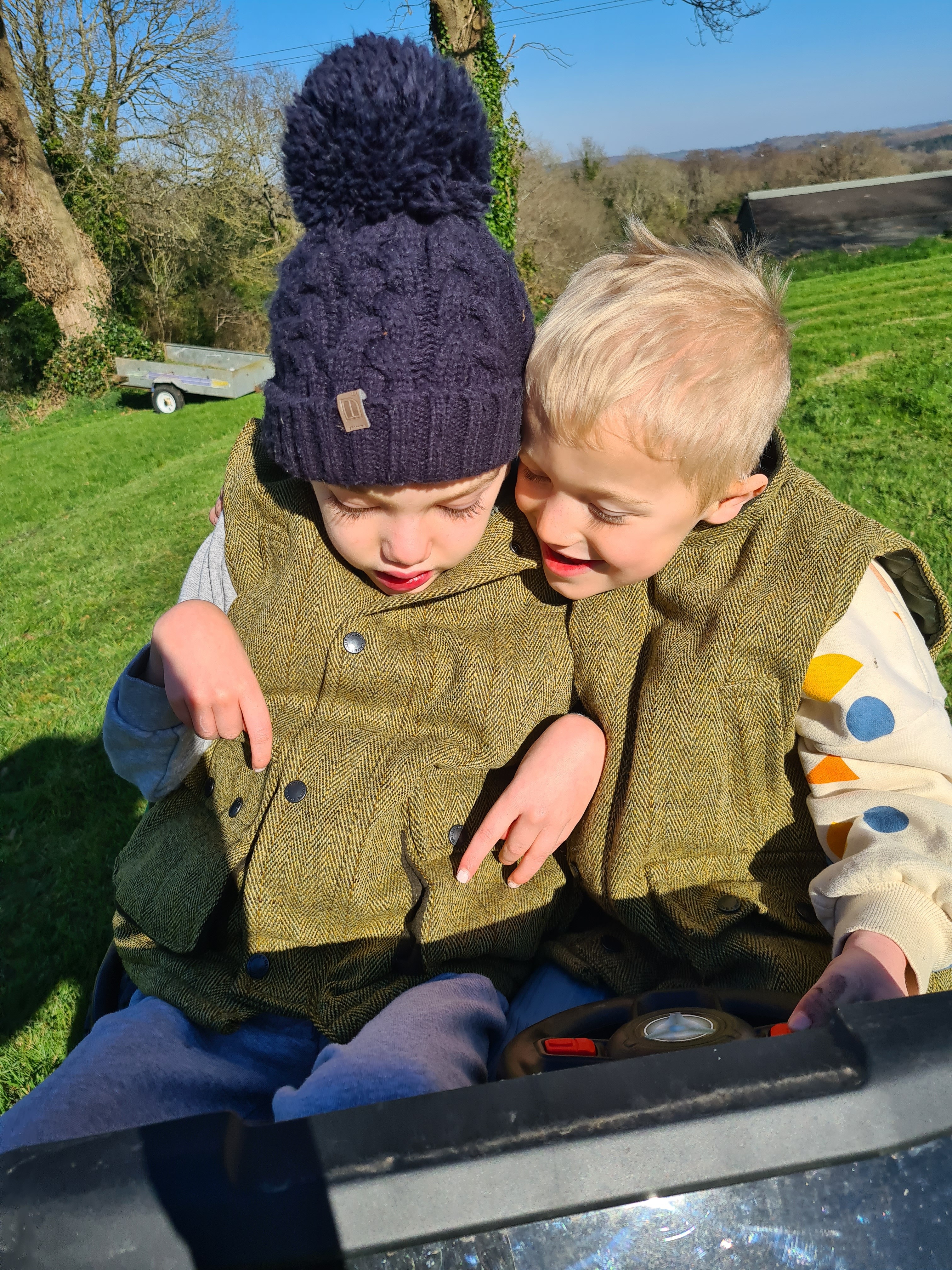 Two brothers outside smiling at each other while riding on a toy car
