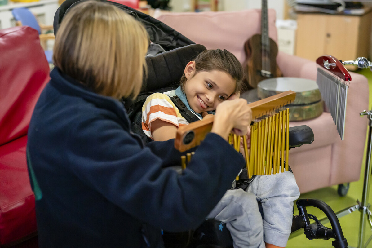 Teddy smiling in his wheelchair while playing a musical instrument at Demelza South East London.