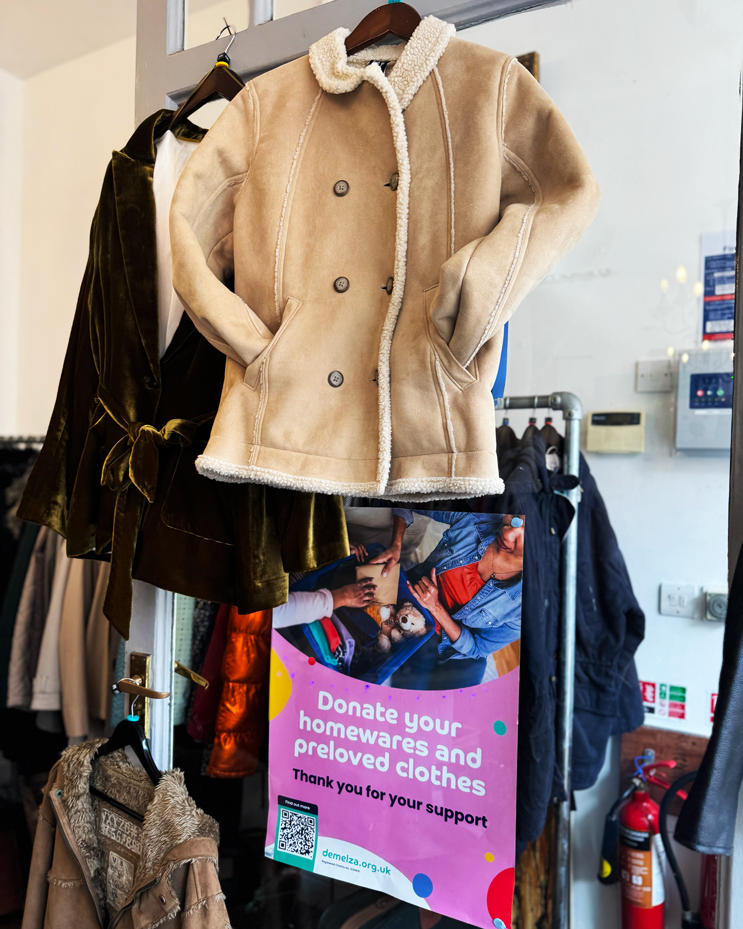 A brown coat with a fur collar hanging up above a rail of different shirts and coats at Rochester's Demelza charity shop