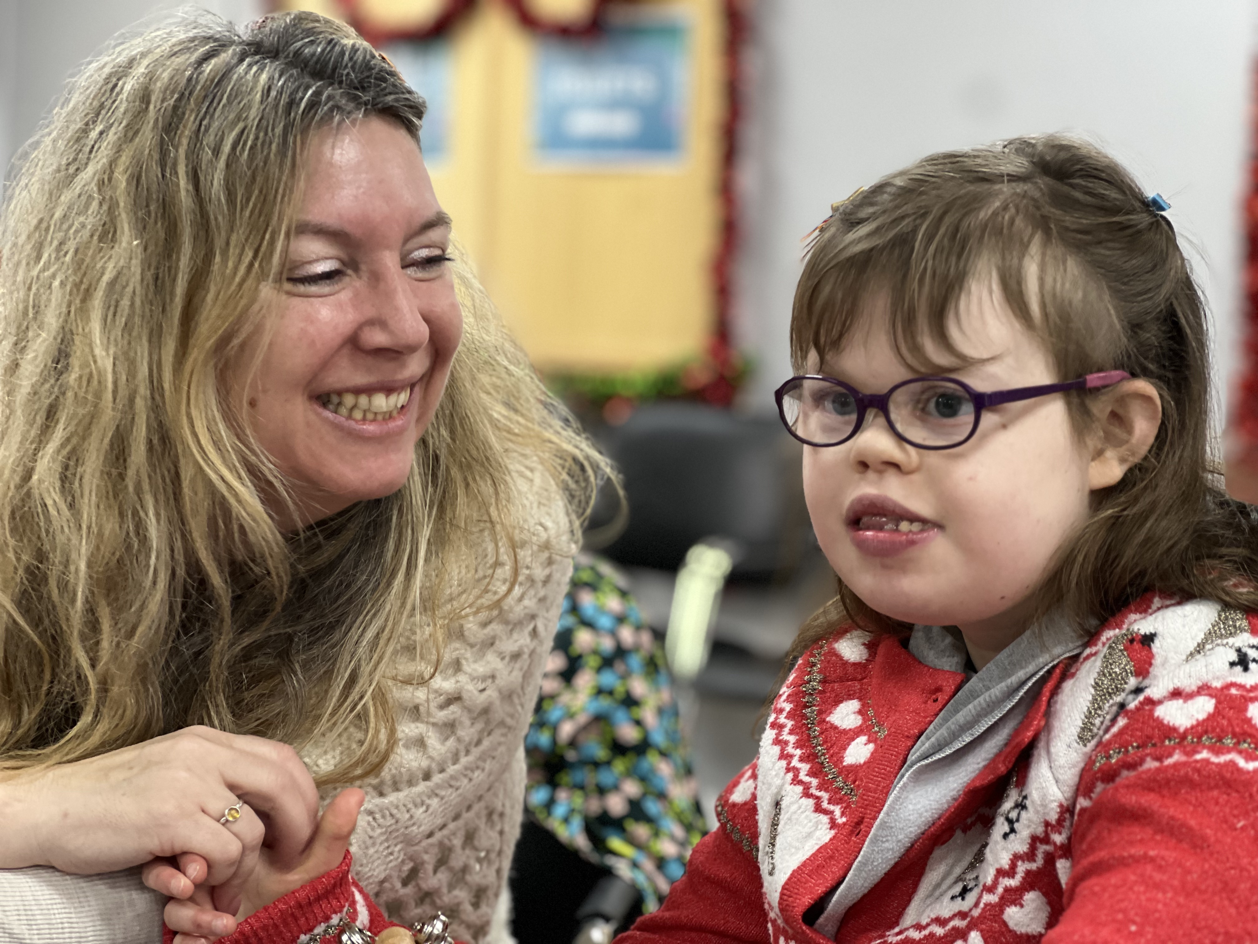 A woman with blonde hair smiling at a child with glasses in a Christmas jumper