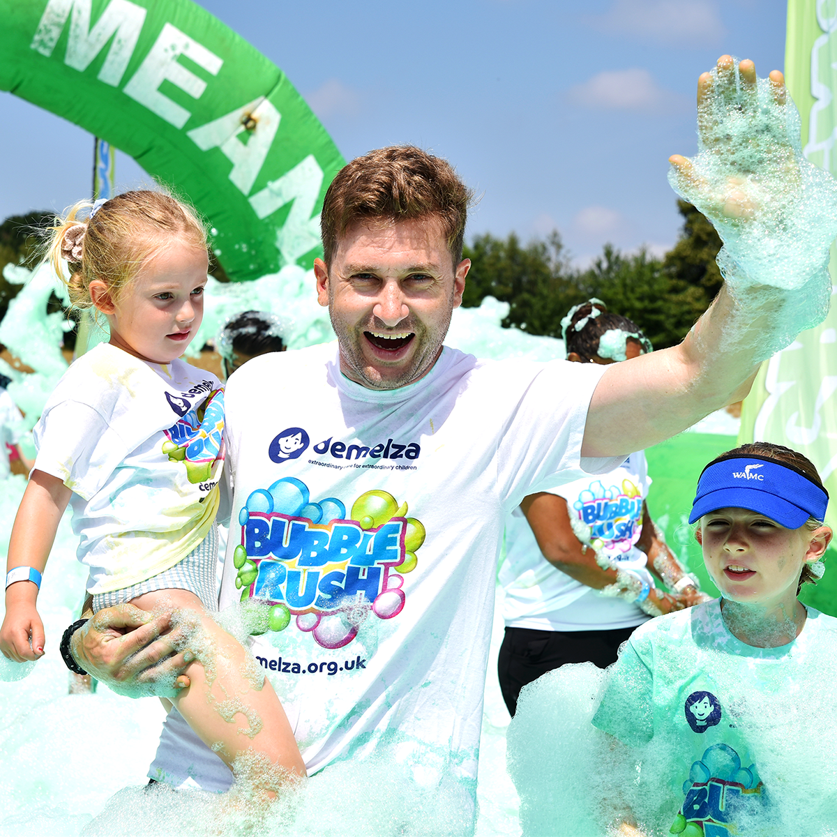 An image of an older man covered in green bubbles holding a young girl up to his shoulders