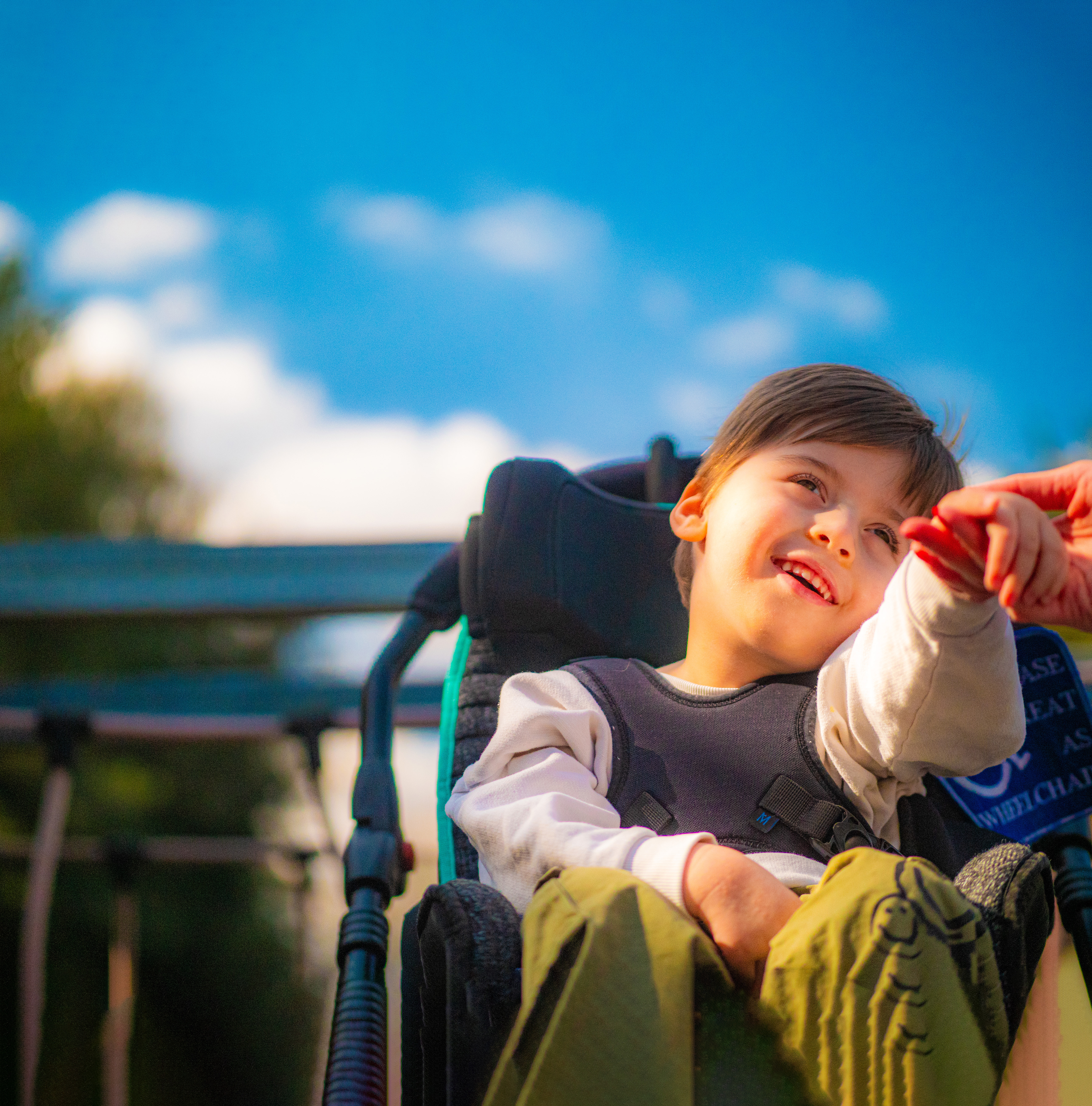 A young boy in a wheelchair holding his mother's hand