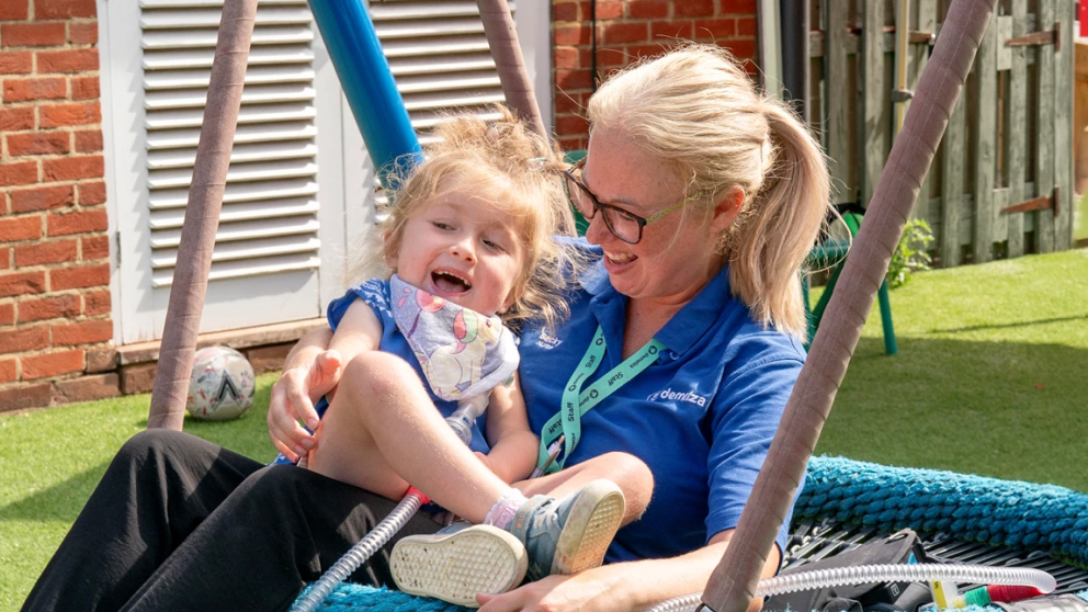 A nurse with blonde hair holding a young girl on the swing while both smiling