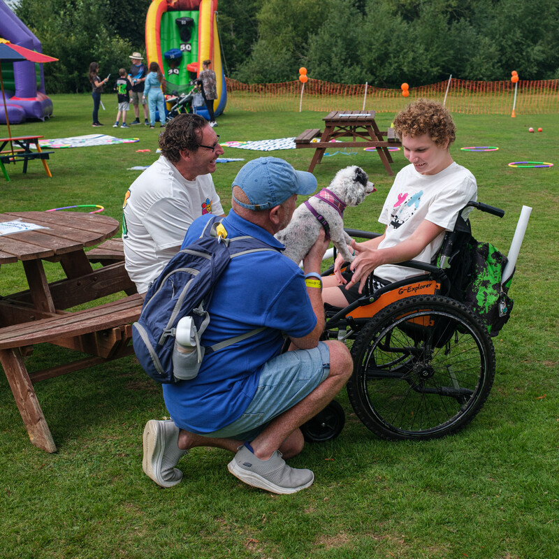 Mason, seated in his wheelchair, smiles as a PAT dog rests on his lap during Kent Family Fest 2025, surrounded by family outdoors.