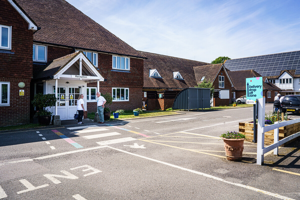 Two Demelza staff members talk outside the main reception at Kent, near the car park on a bright day.