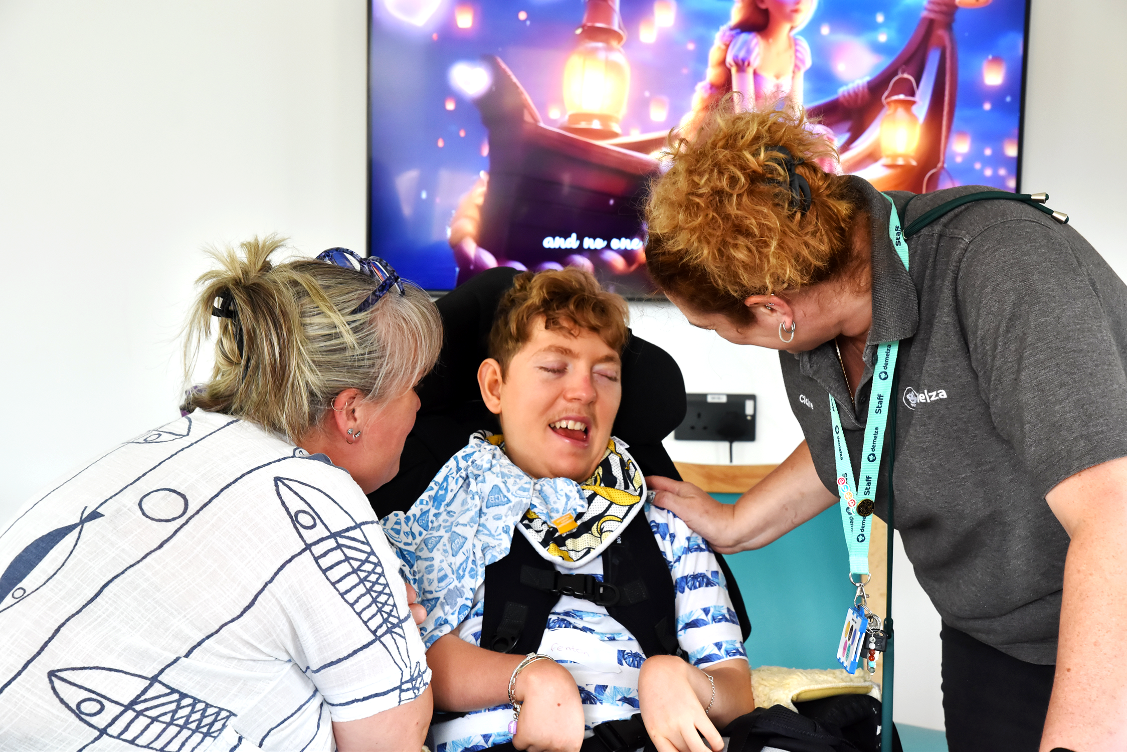 Two women looking at a young person in a wheelchair who's smiling