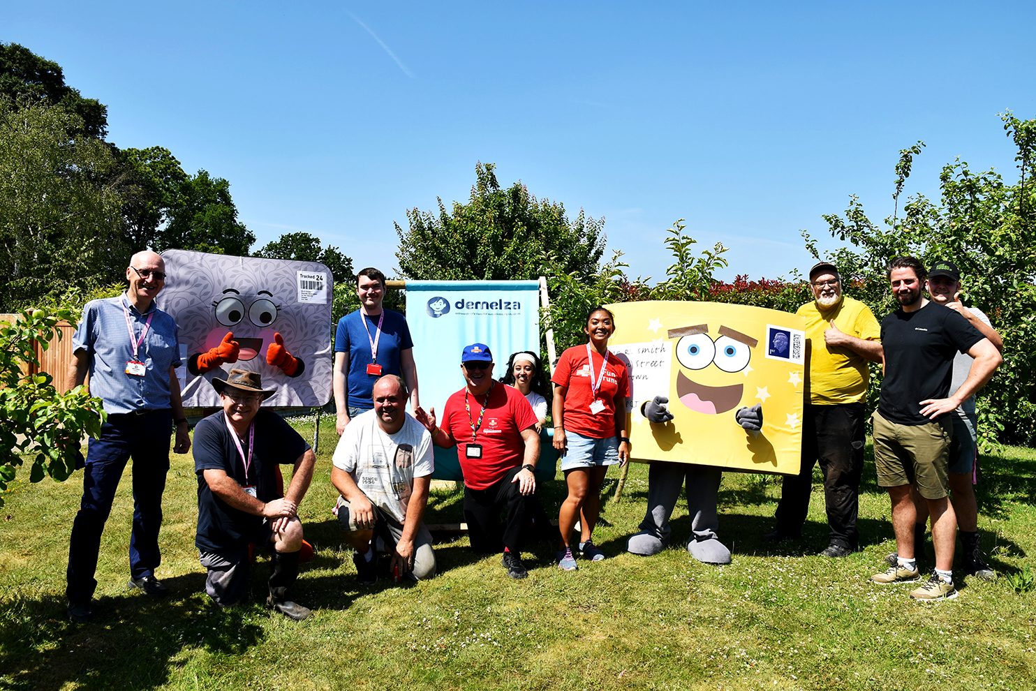 Royal Mail volunteers and two mascots stand together in a sunny garden at Demelza Kent.