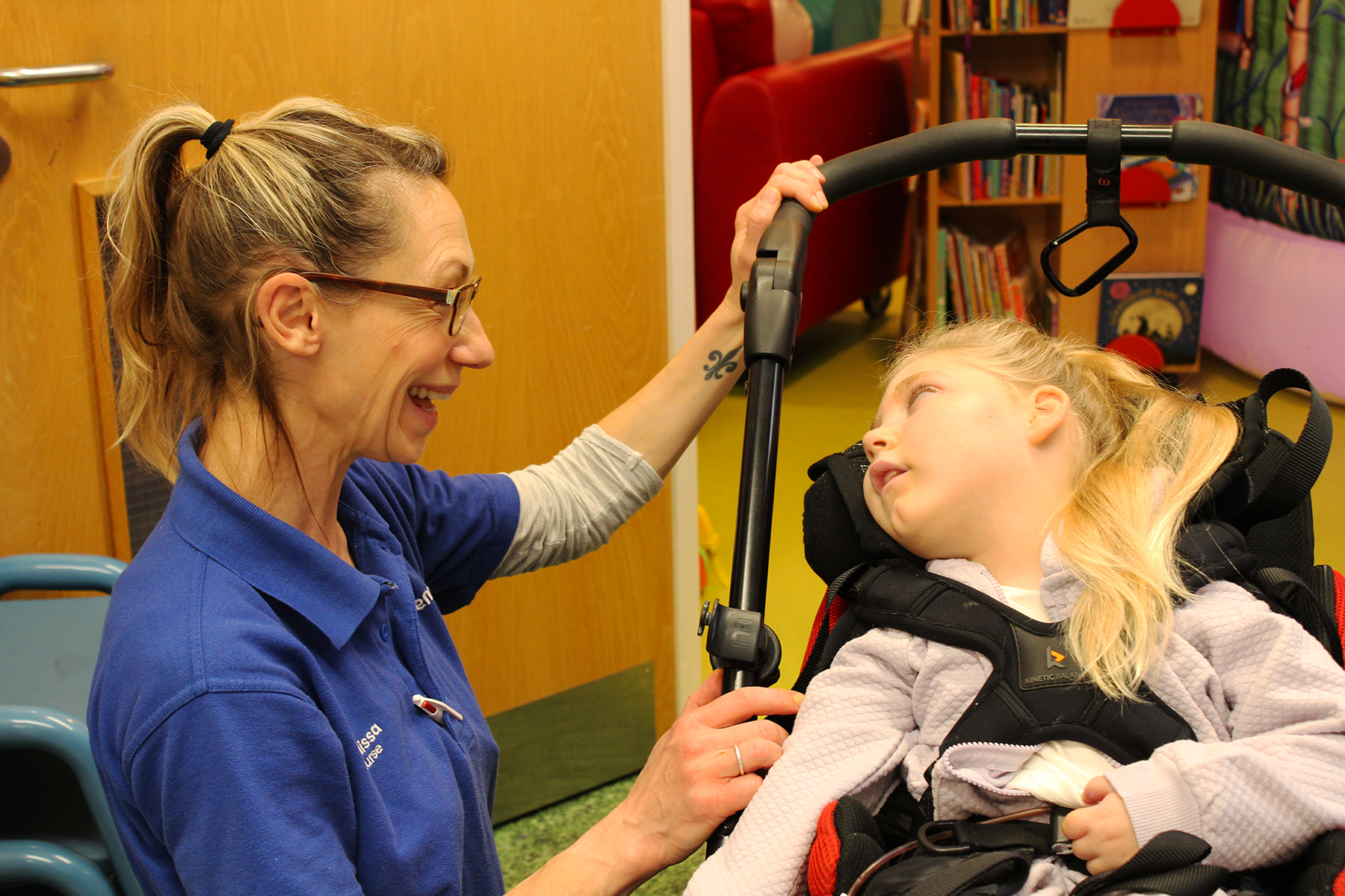 A nurse with glasses smiling towards a child in a wheelchair