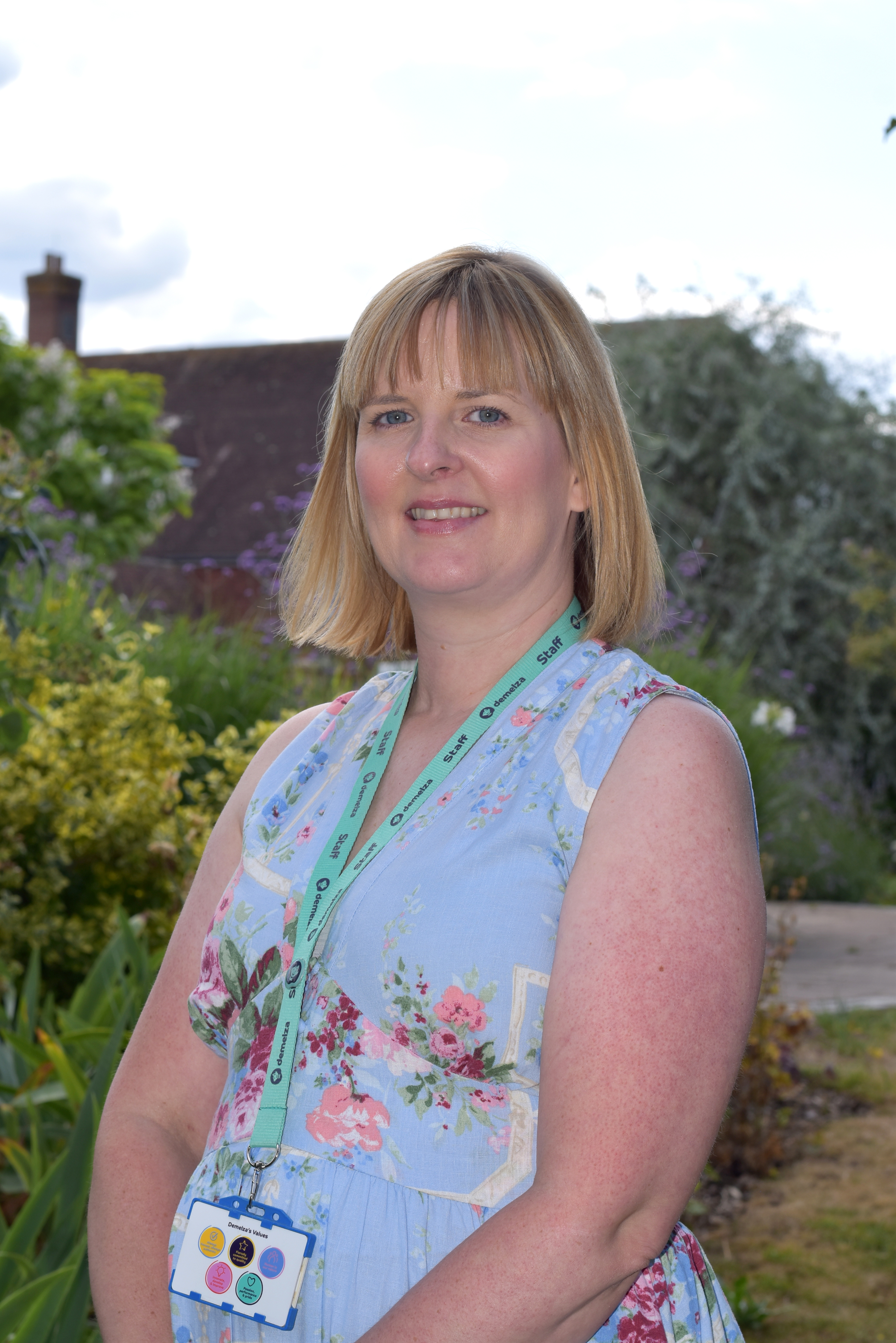 Claire Ellis-Waghorn, Director of IT, Data and Governance, stands in Demelza’s gardens wearing a blue floral dress
