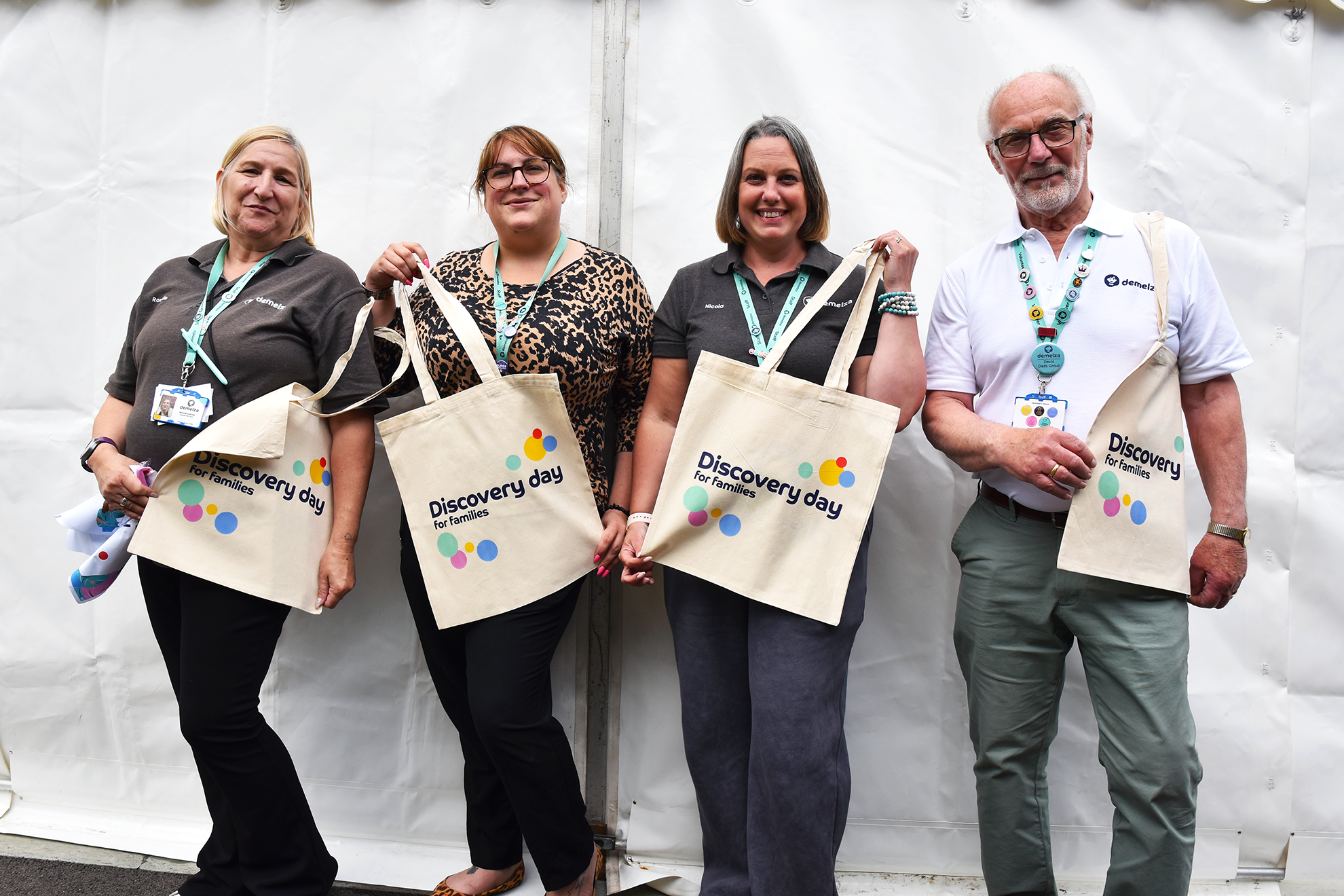 Staff and volunteers hold Demelza tote bags outside a white marquee at Family Discovery Day 2025, smiling and ready to greet guests.
