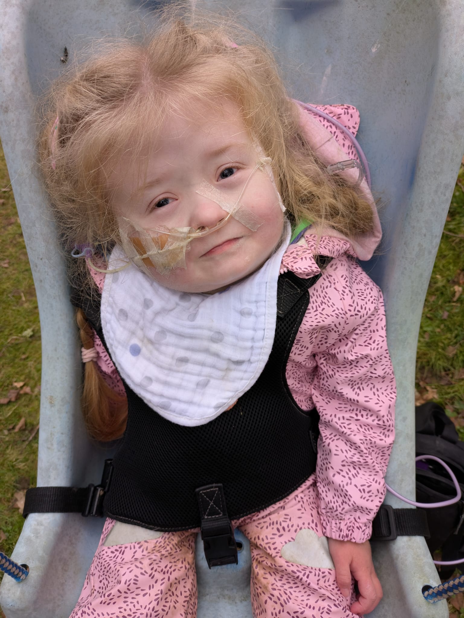 A young child with a breathing tube sitting in a chair looking into the camera