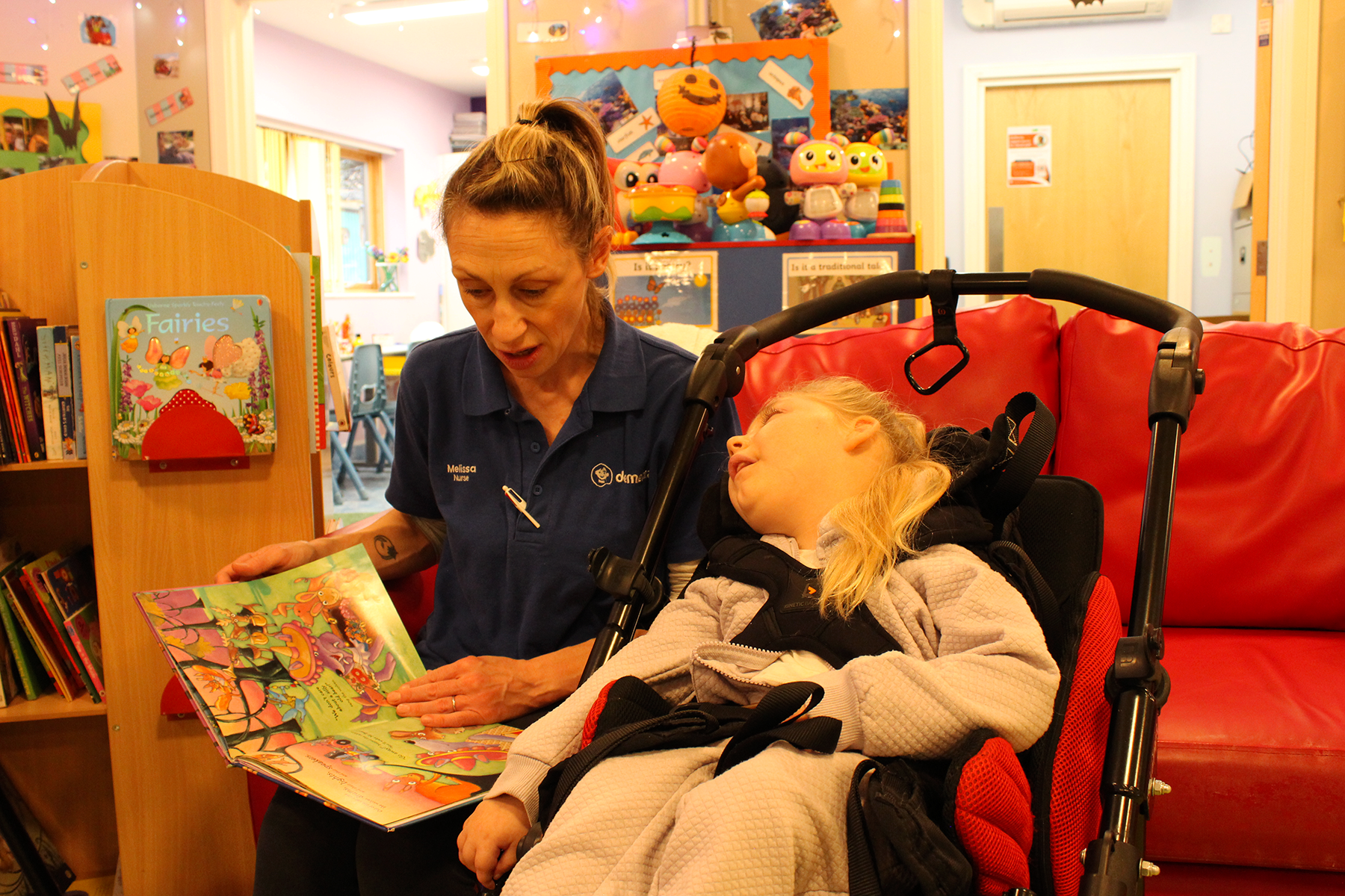 A nurse reading a storybook to a young girl in a wheelchair at Demelza SEL