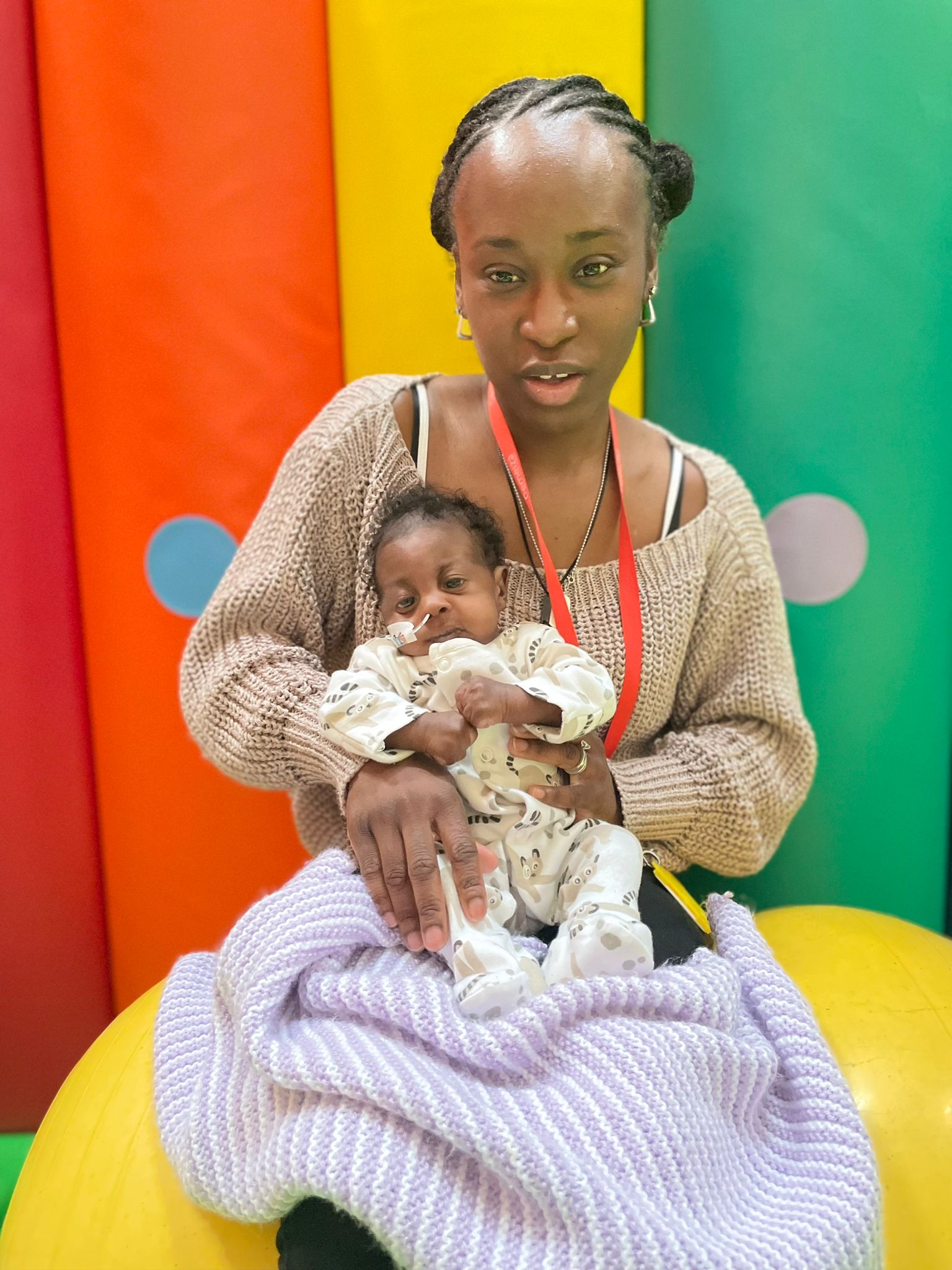 A woman holding her baby daughter looking towards the camera in Demelza's soft play room