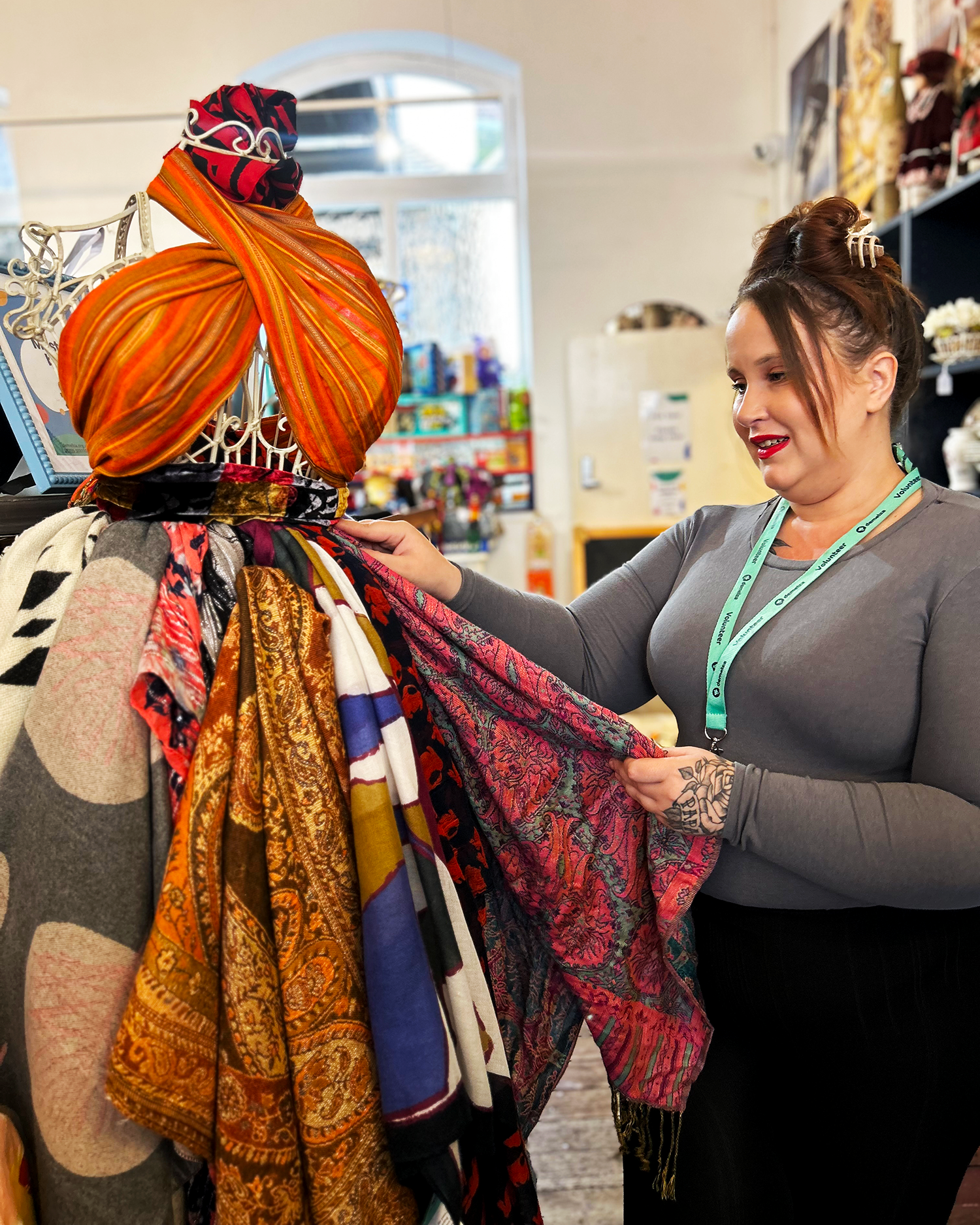 Lady with grey top and hair tied up arranging a clothing display in a charity shop