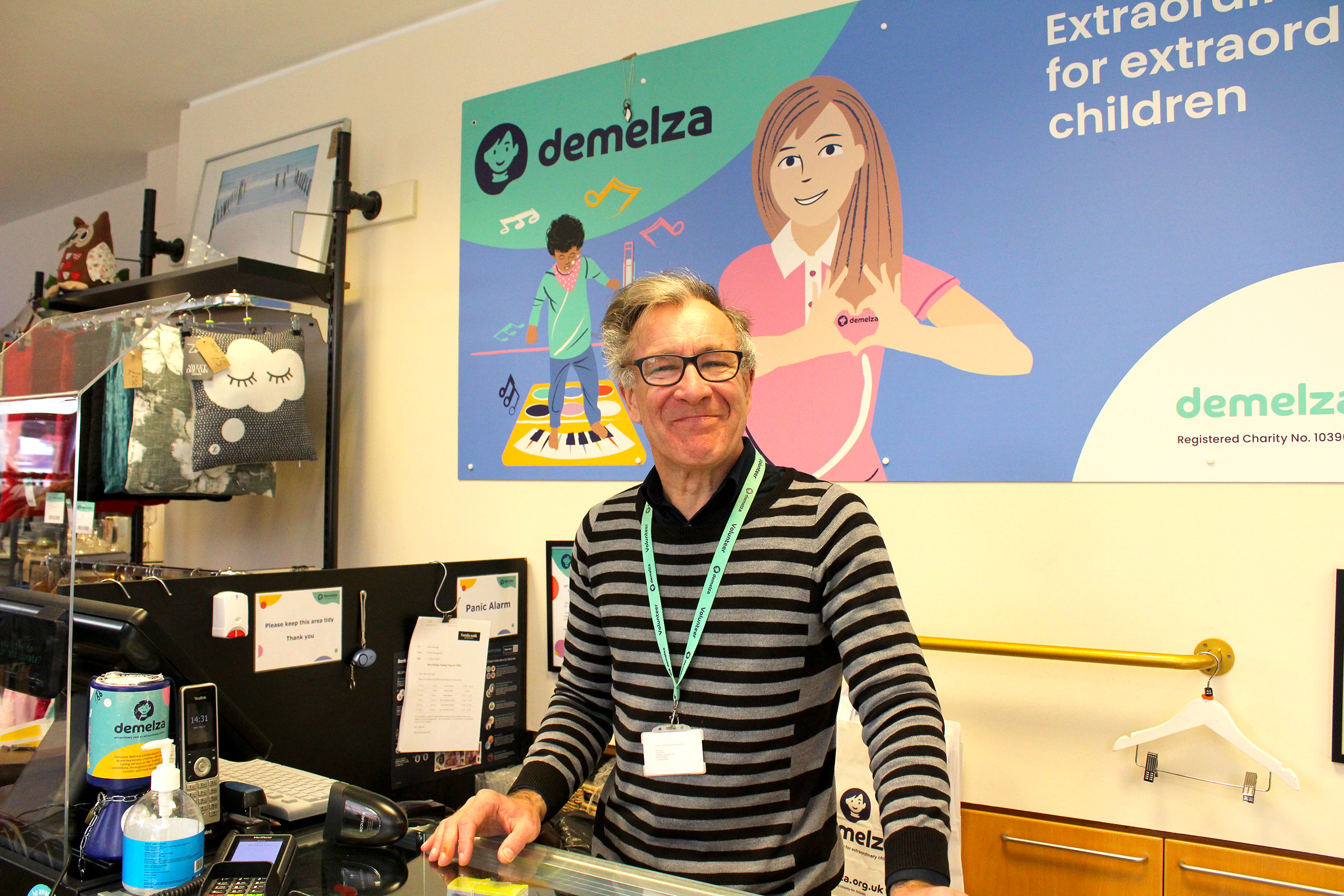 Retail volunteer Nathan at the Maidstone Earl Street shop till, wearing a striped top and smiling warmly.