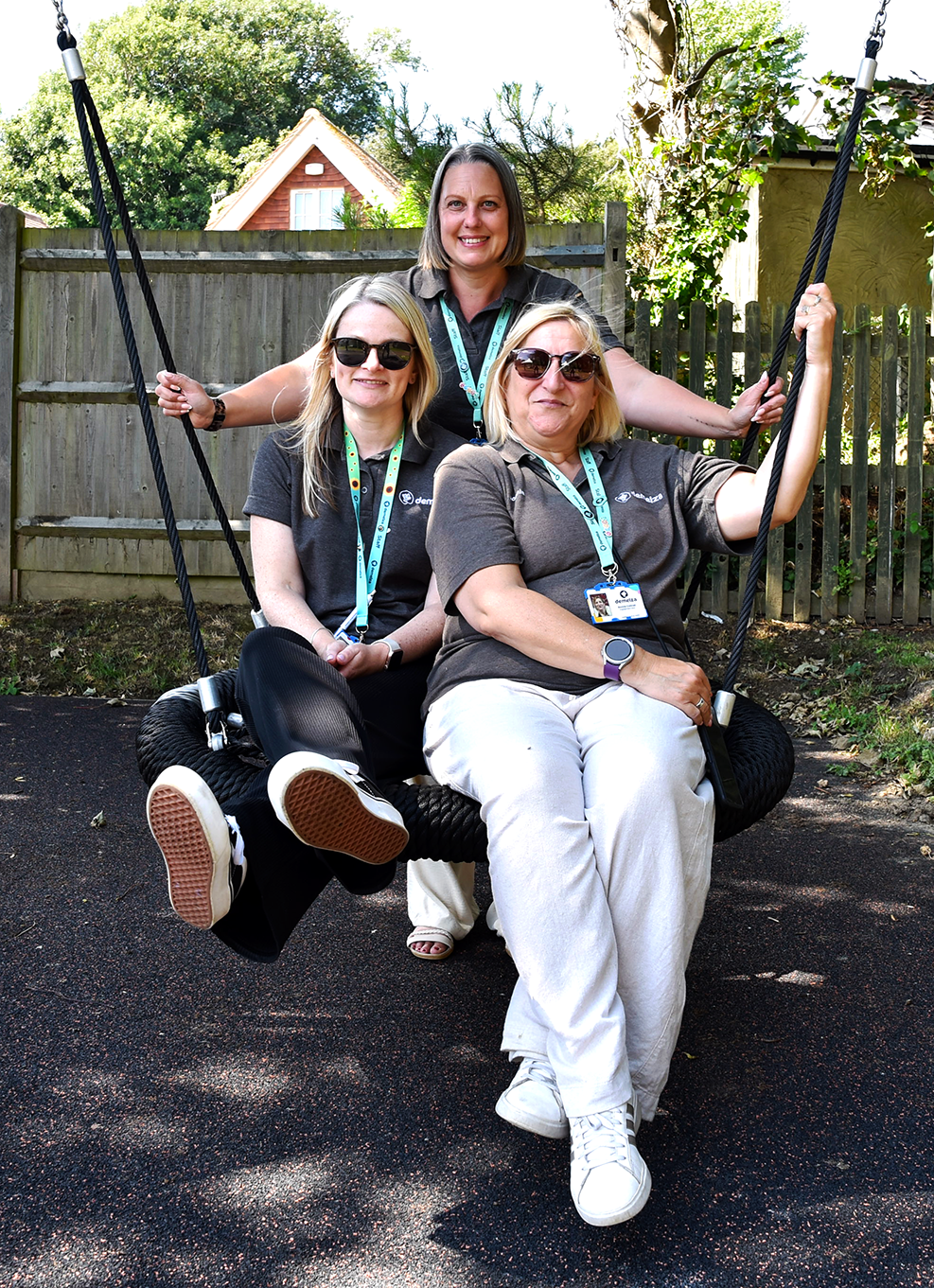 Three East Sussex family engagement team members sit on a swing in a sunny garden, smiling.
