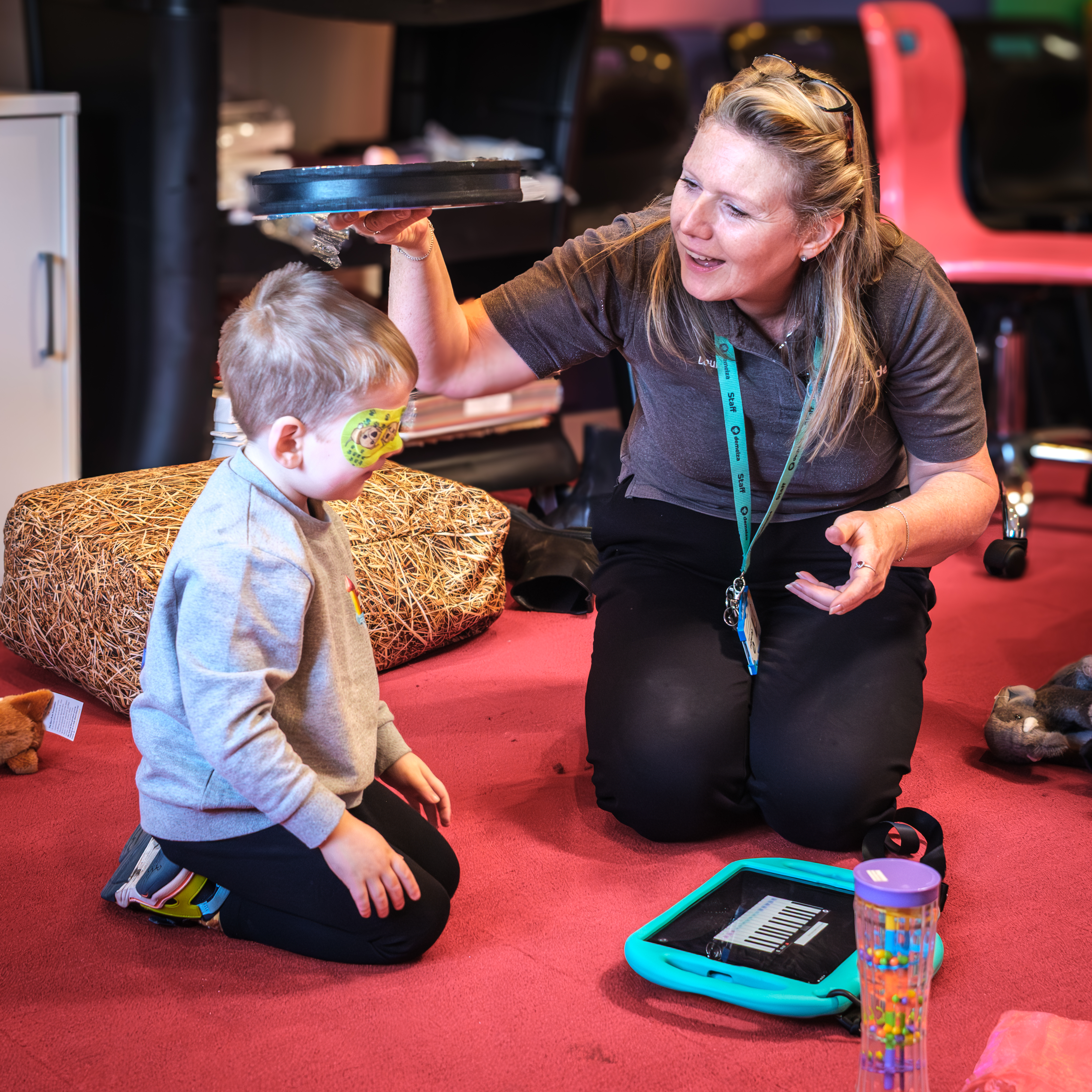 A woman with glasses on her head playing with a young child who has a plaster over his eye